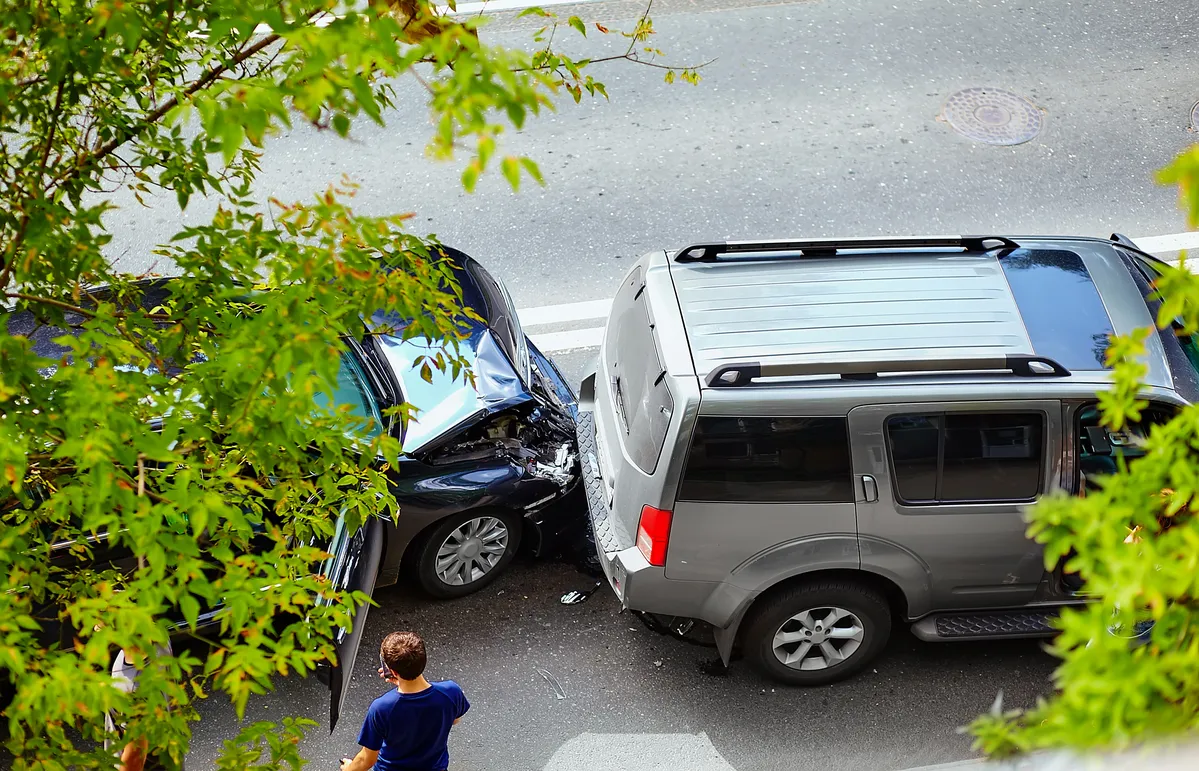 Image of an car accident in the road with trees slightly blocking the view