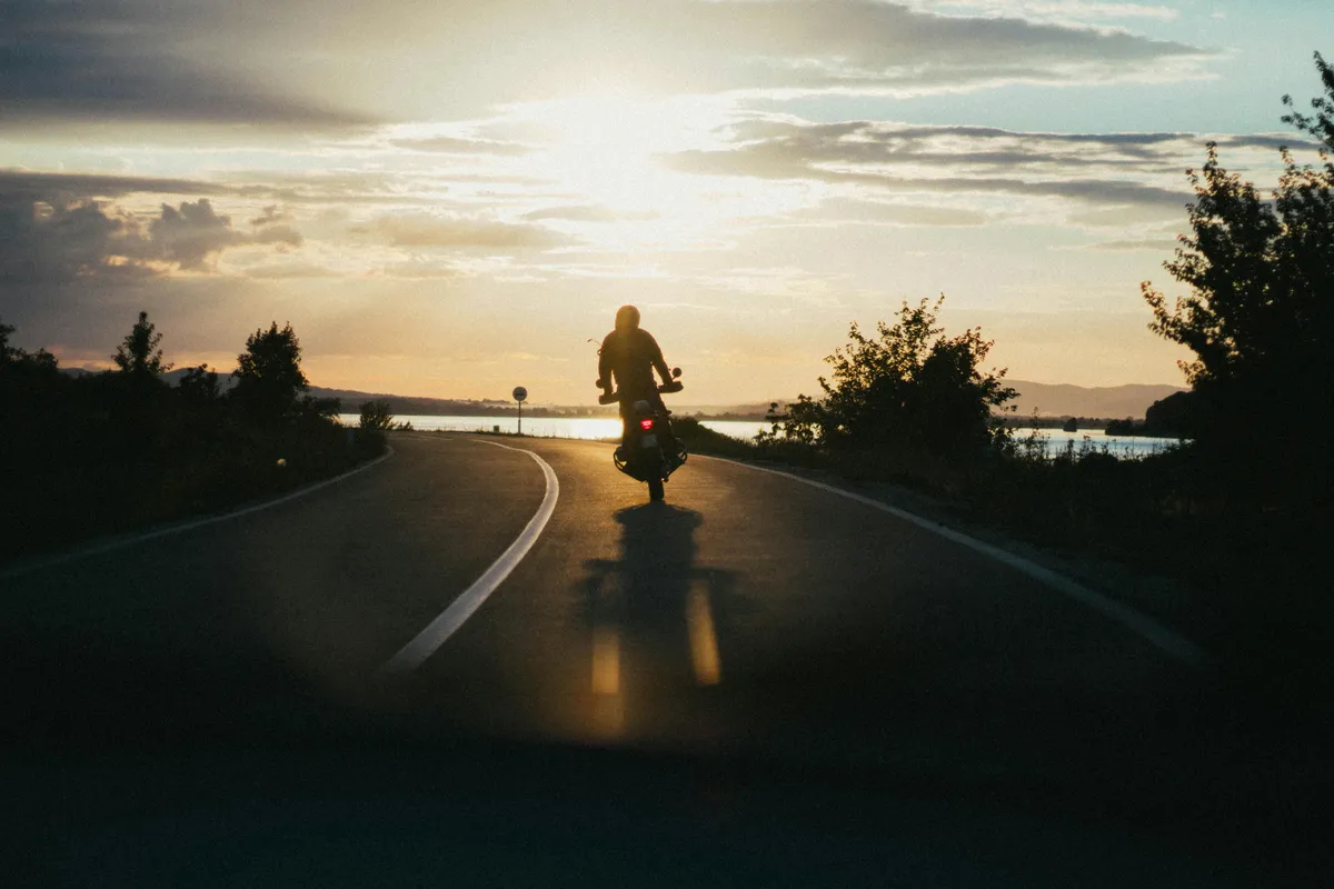  a man riding a motorcycle down the road at sunset