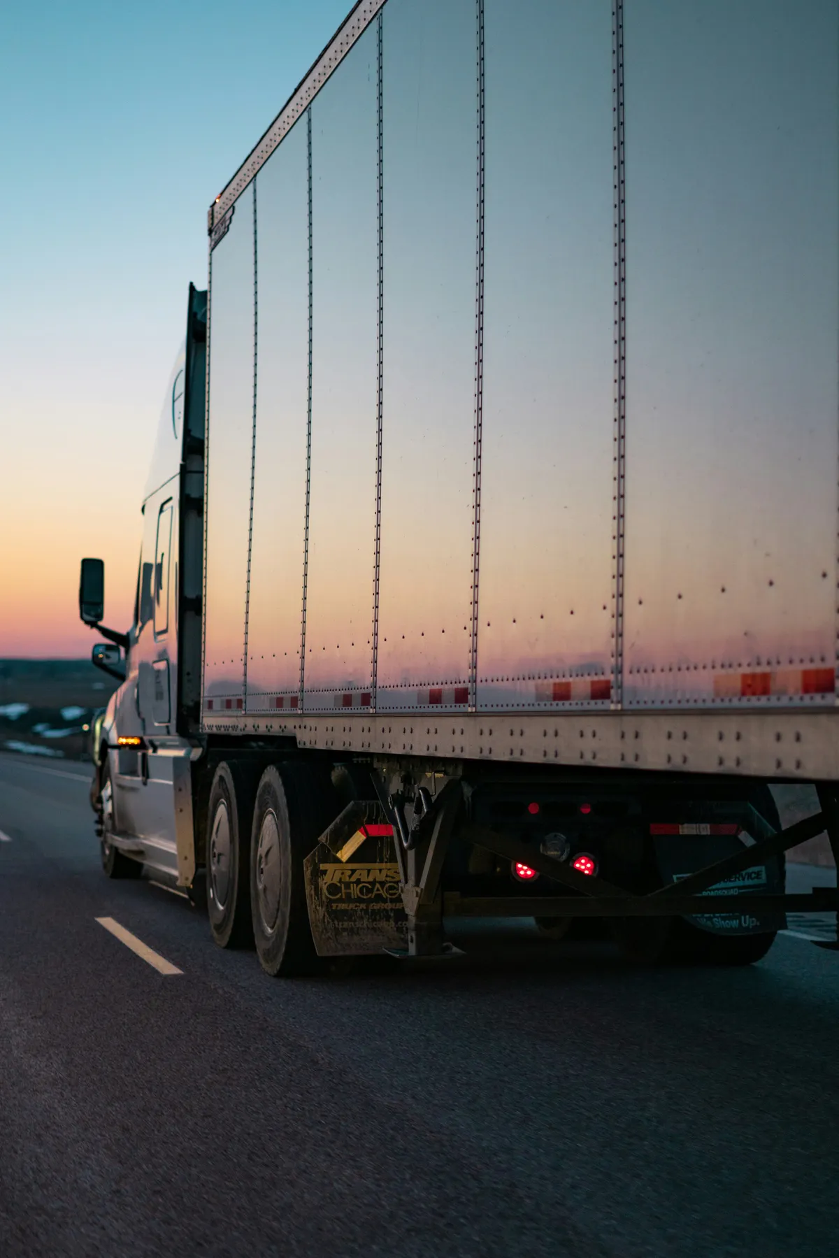  a semi truck driving down the highway at dusk