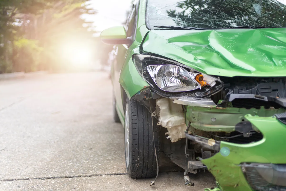 arafed green car with front bumper damage on the side of the road