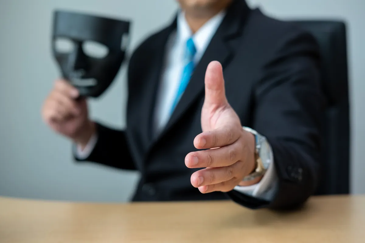 arafed man in a suit and tie holding a mask and giving a thumbs up