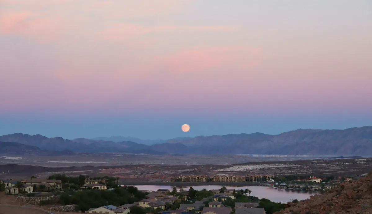 arafed view of a full moon rising over a town with a lake