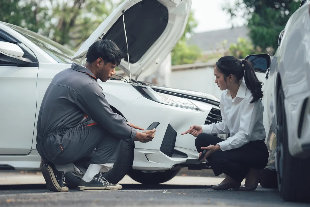 araffes looking at a cell phone while a man checks the tire