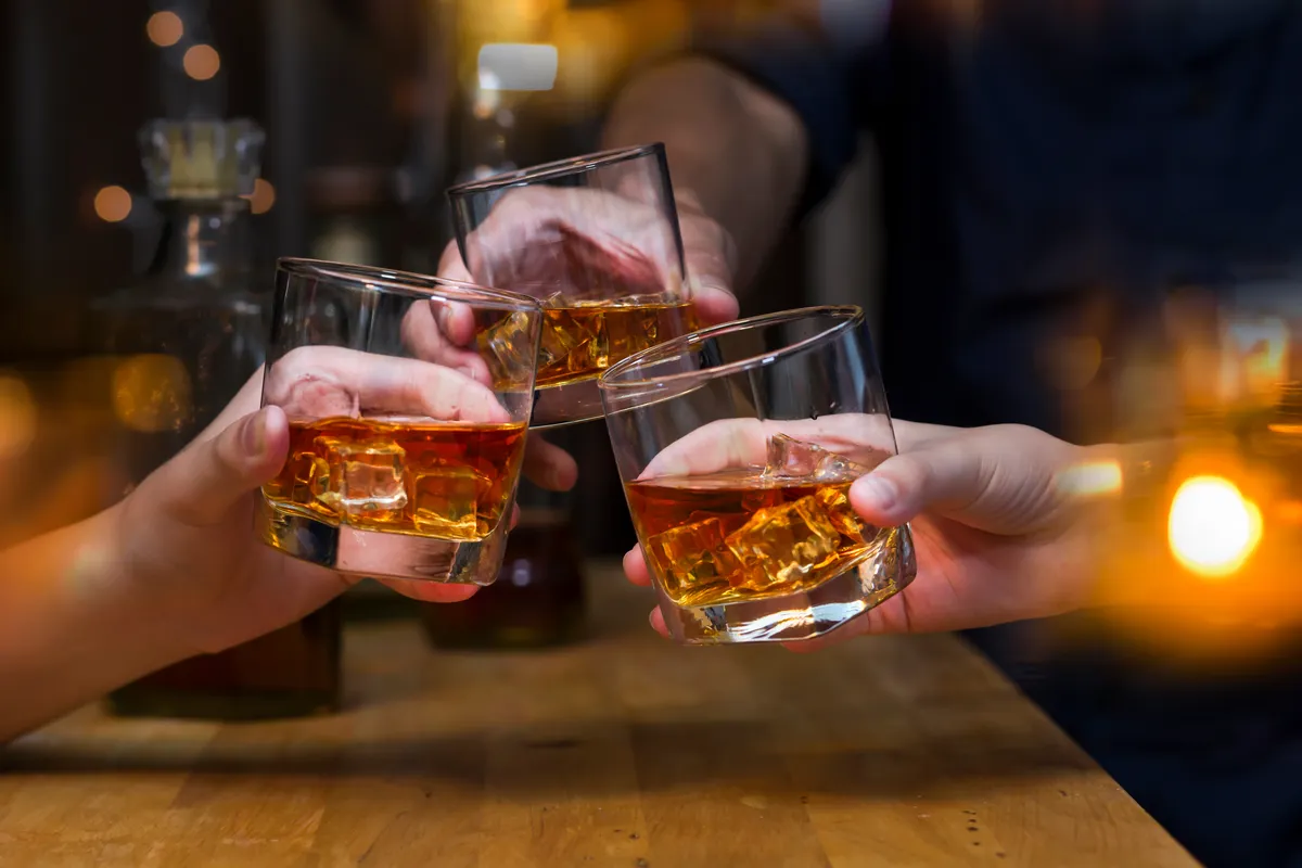 people holding glasses of whiskey toasting at a bar