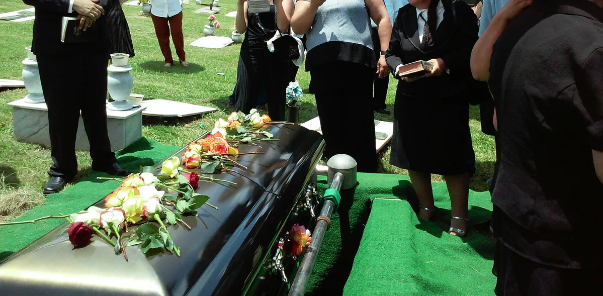people standing around a black casket with flowers on it
