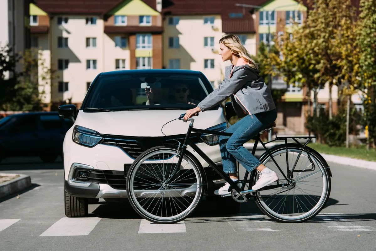 woman riding a bike in the street with a car behind her